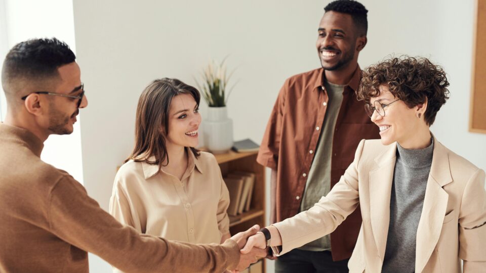 Four colleagues smiling and shaking hands in a bright office setting.